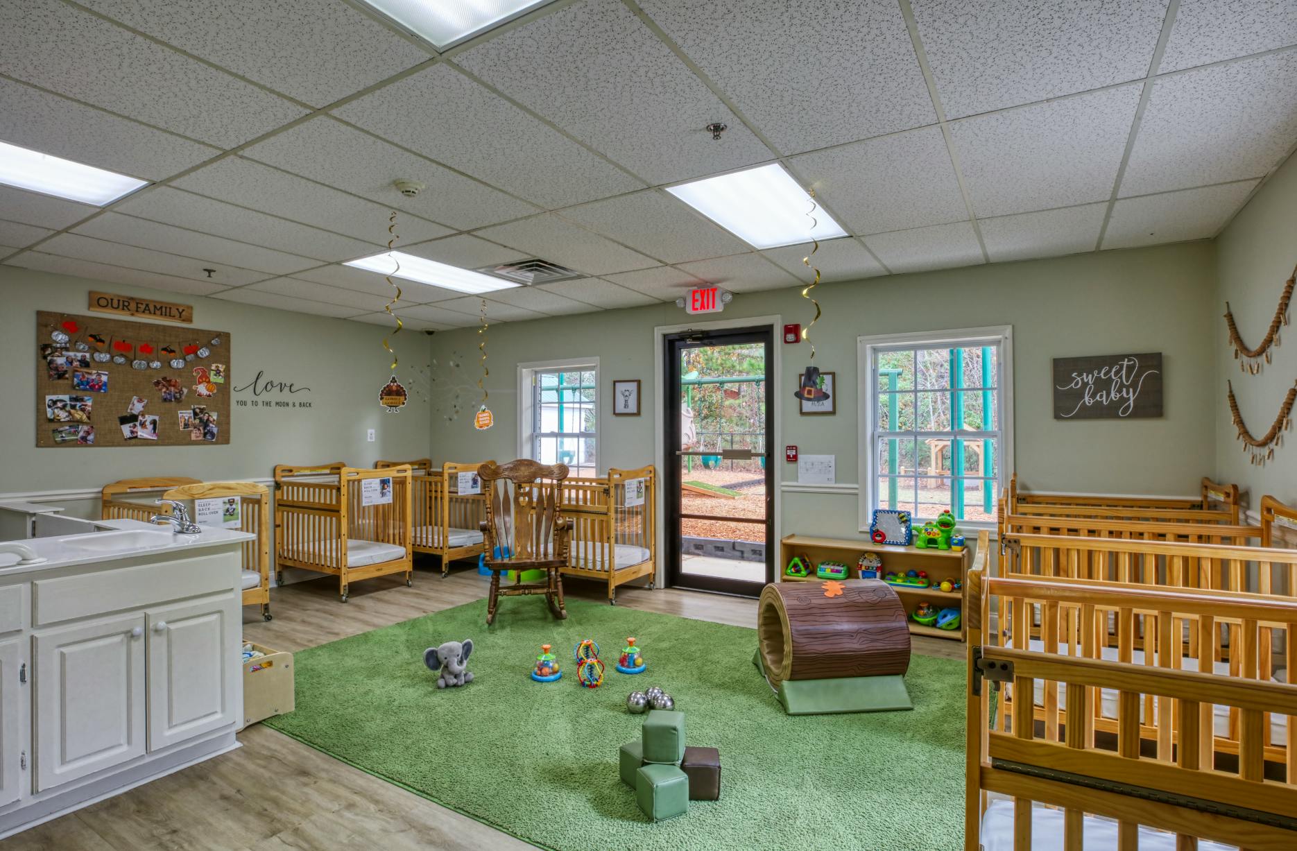 Cribs, rocking chair, and toys in a bright room with a green carpeted area