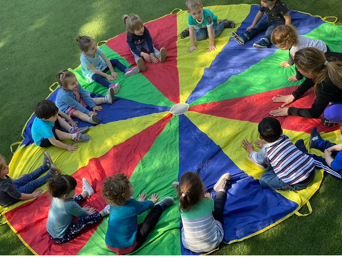 Children and adults sitting on a colorful parachute on grass
