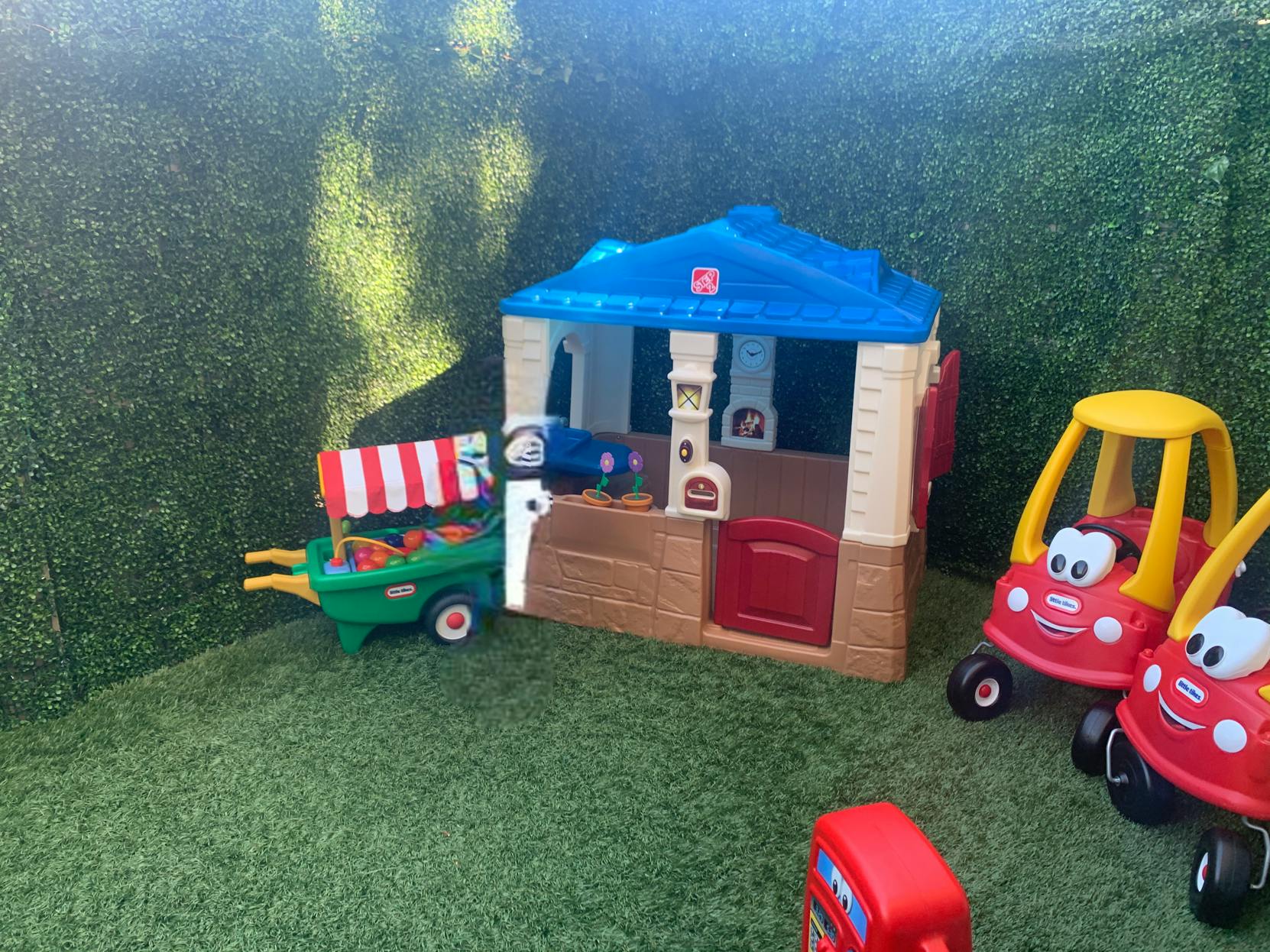 Toy playhouse, toy food cart, and toy cars on artificial grass