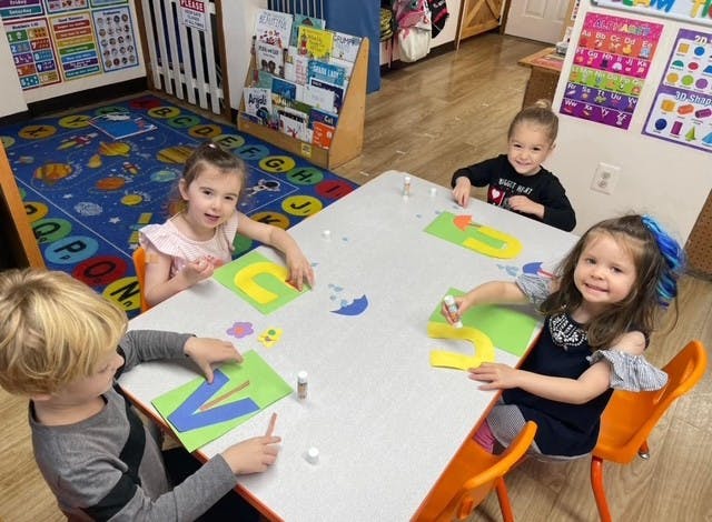 Four children sitting at a table in a classroom doing a paper craft project