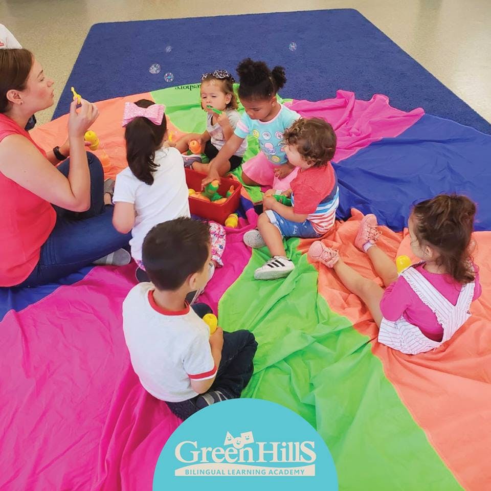 Person blowing bubbles for a group of children on a colorful mat