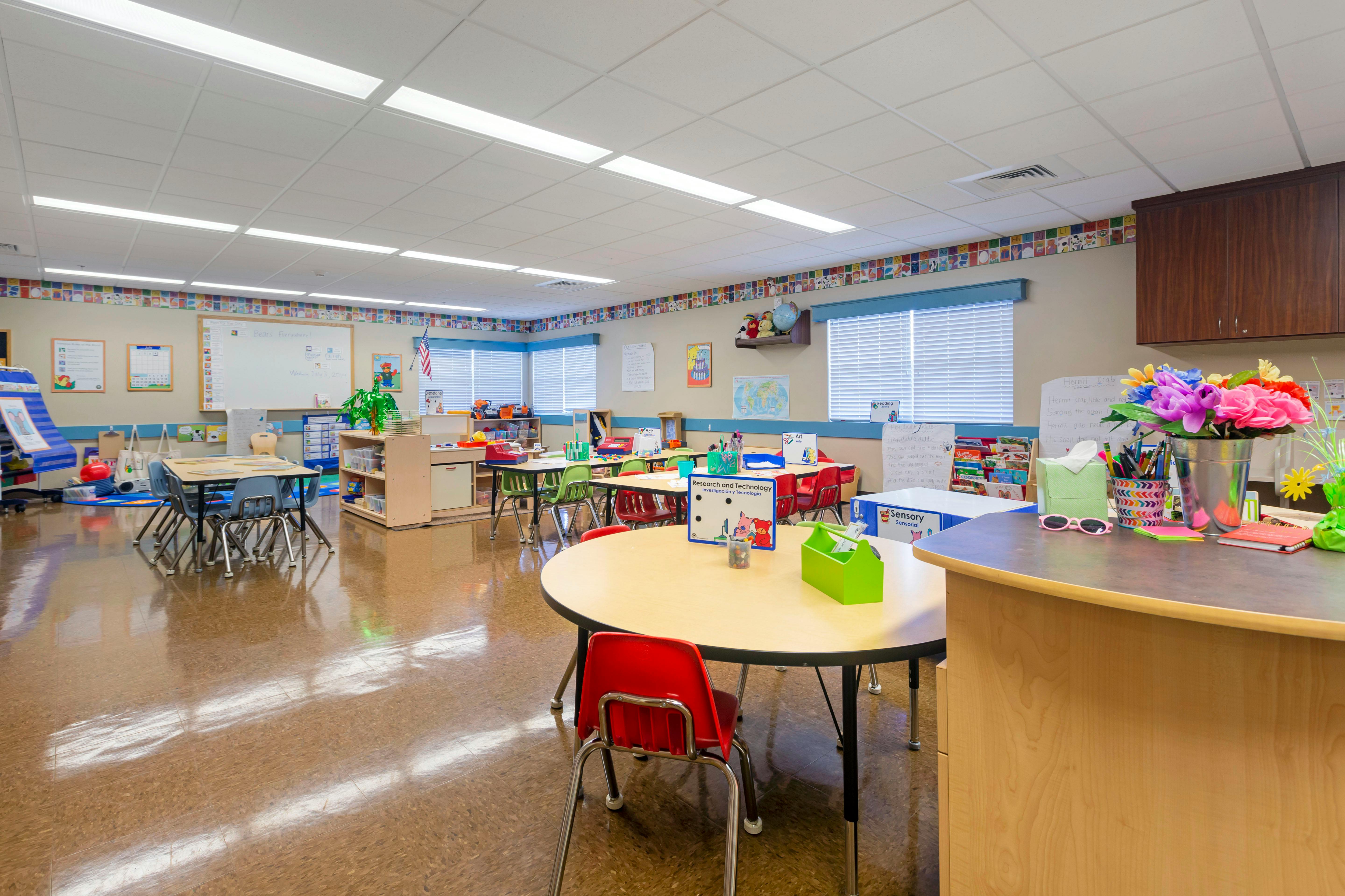 Classroom with multiple small tables and chairs, and a whiteboard