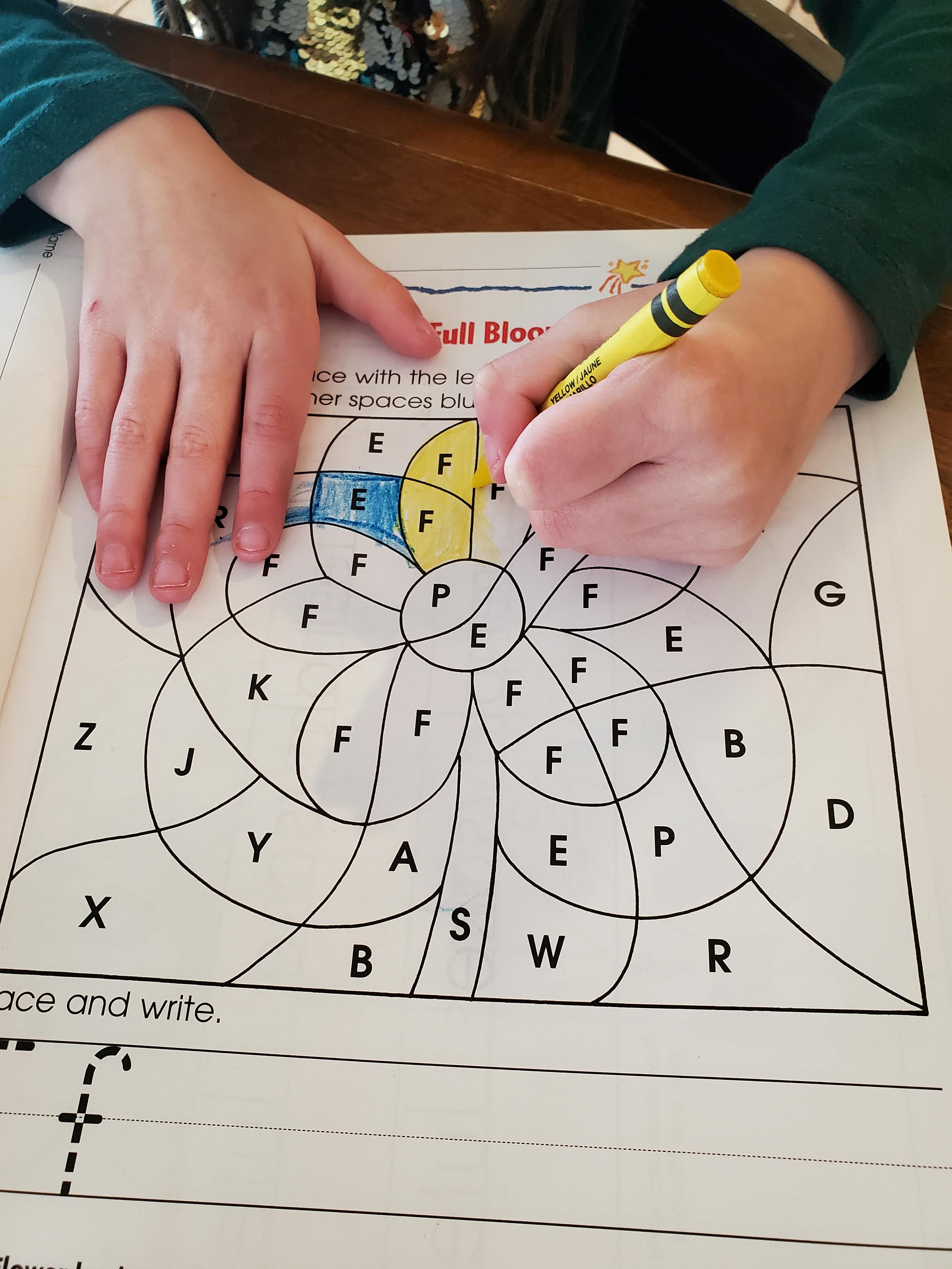 Child coloring a worksheet with letters and shapes