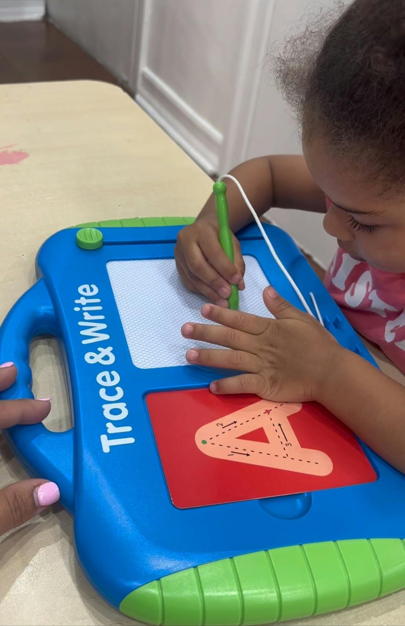 Child tracing the letter A on a "Trace & Write" learning toy