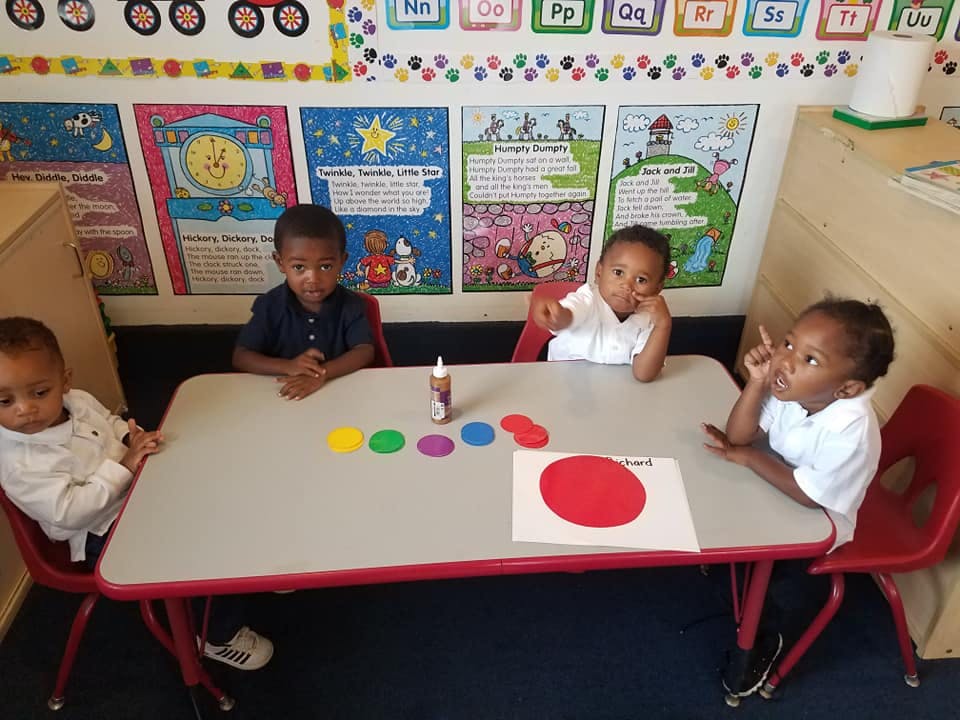 Four children sitting at a table with colorful shapes and glue