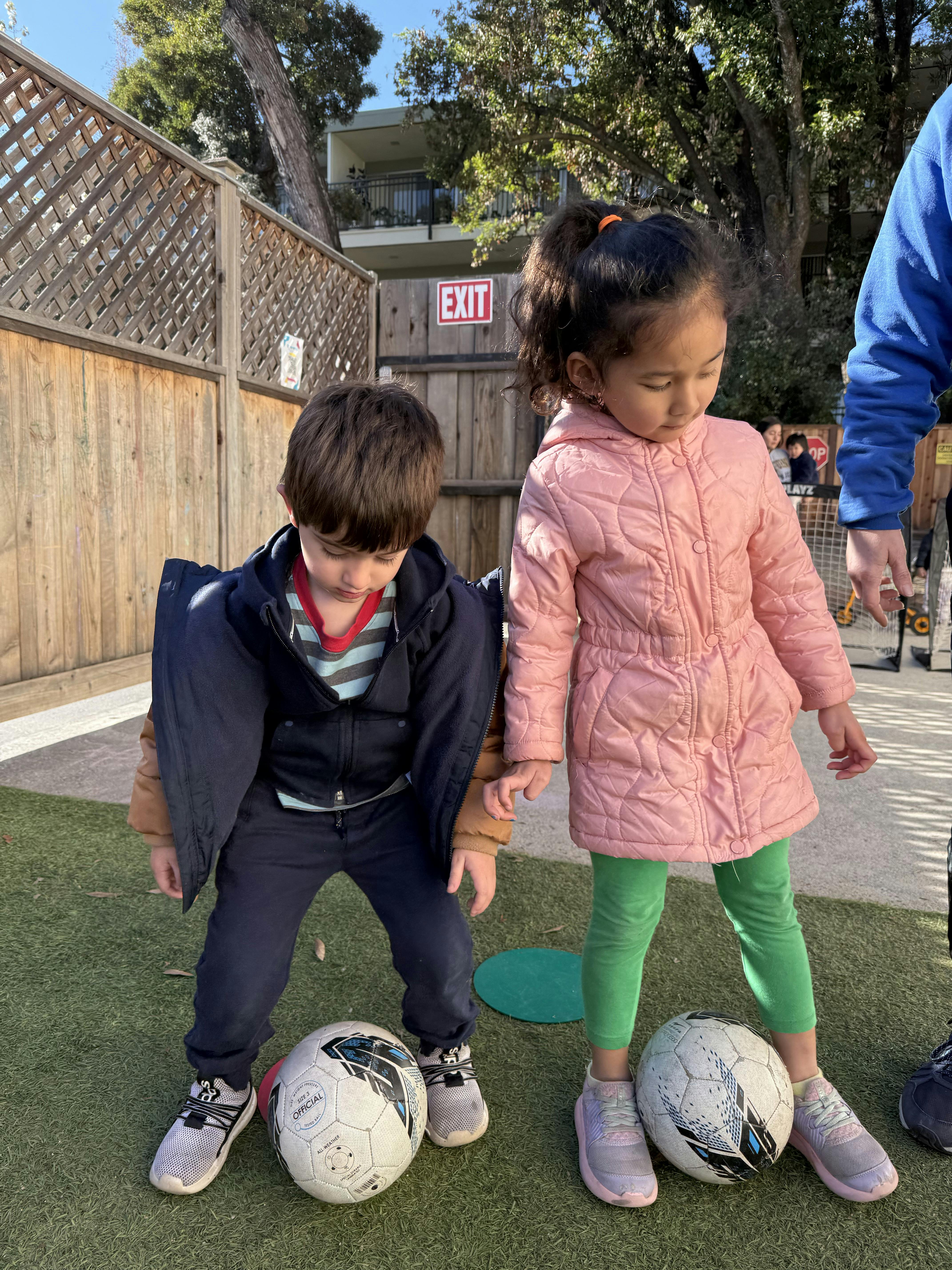 Two children standing with soccer balls on a grassy surface