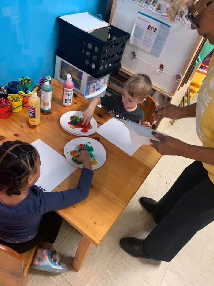 Two children doing an art activity at a table with an adult nearby