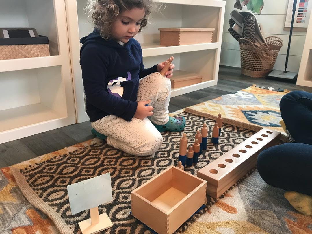 Child kneeling on a rug playing with wooden blocks and pegs