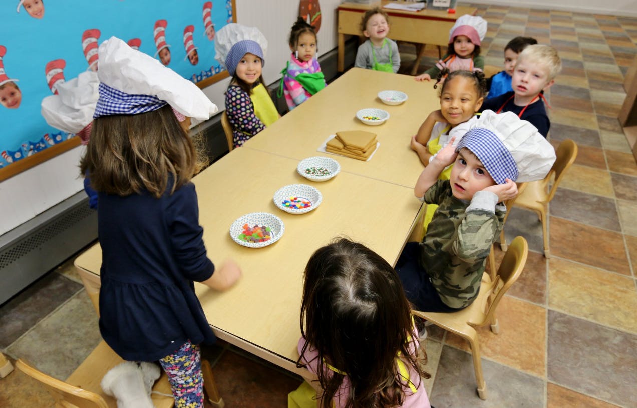 Children wearing chef hats sitting at a table with bowls of candy