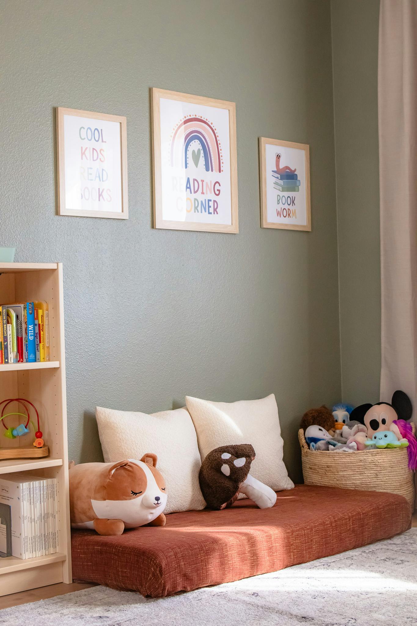 Reading nook with a floor cushion, pillows, stuffed animals, and framed art