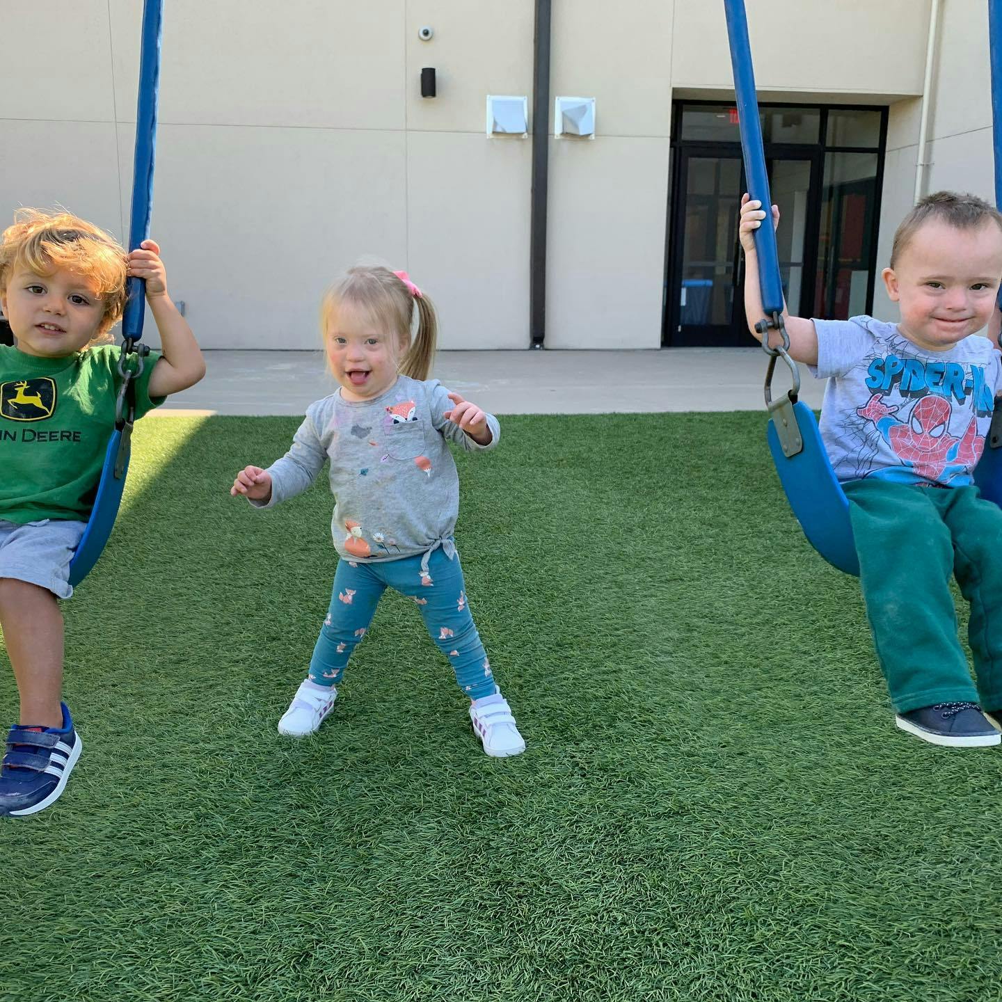 Three children playing on swings and standing on artificial grass