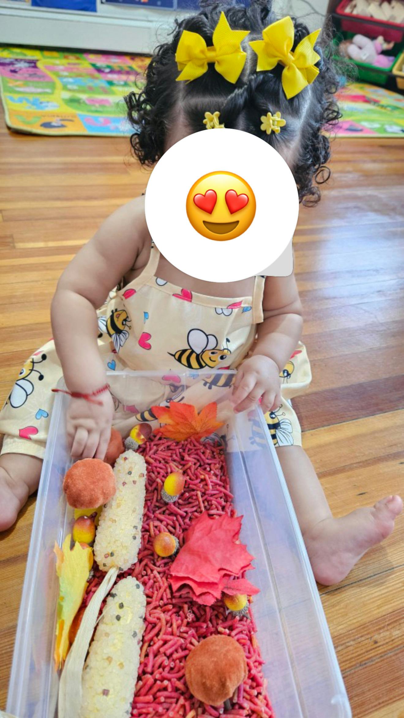 Child playing with a sensory bin filled with red rice and autumn-themed items