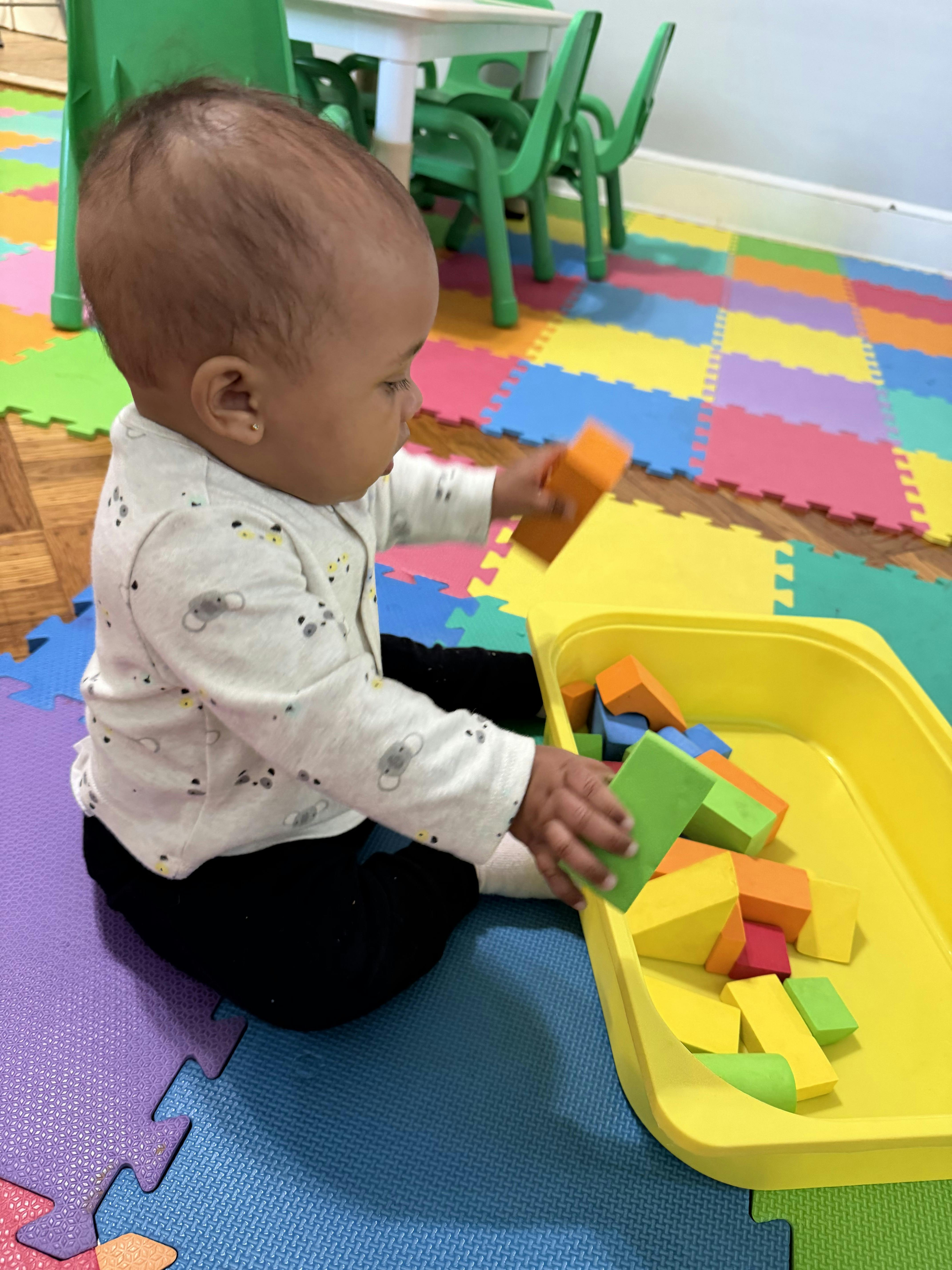 A child playing with toy blocks on a colorful foam floor