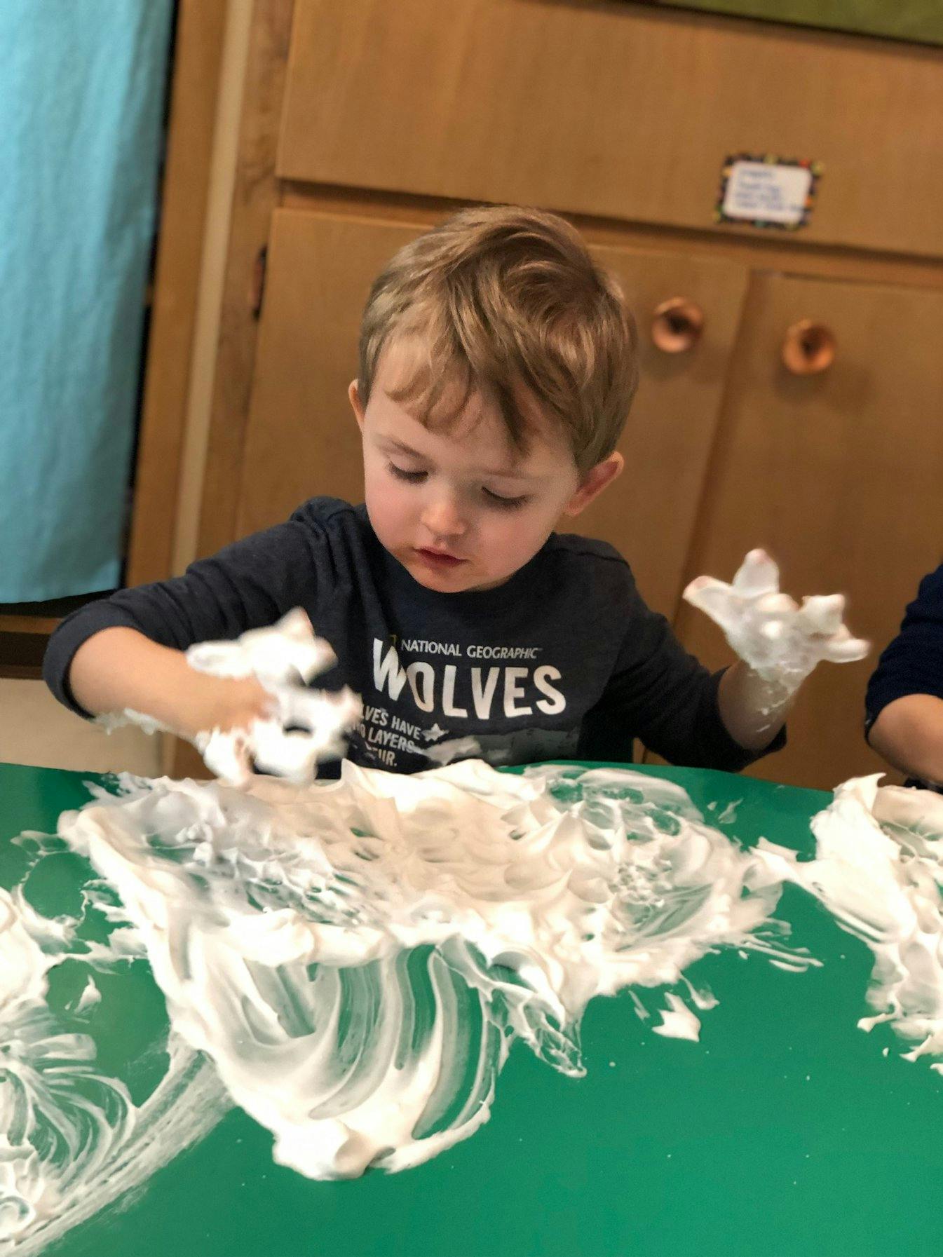 Child playing with shaving cream on a green table