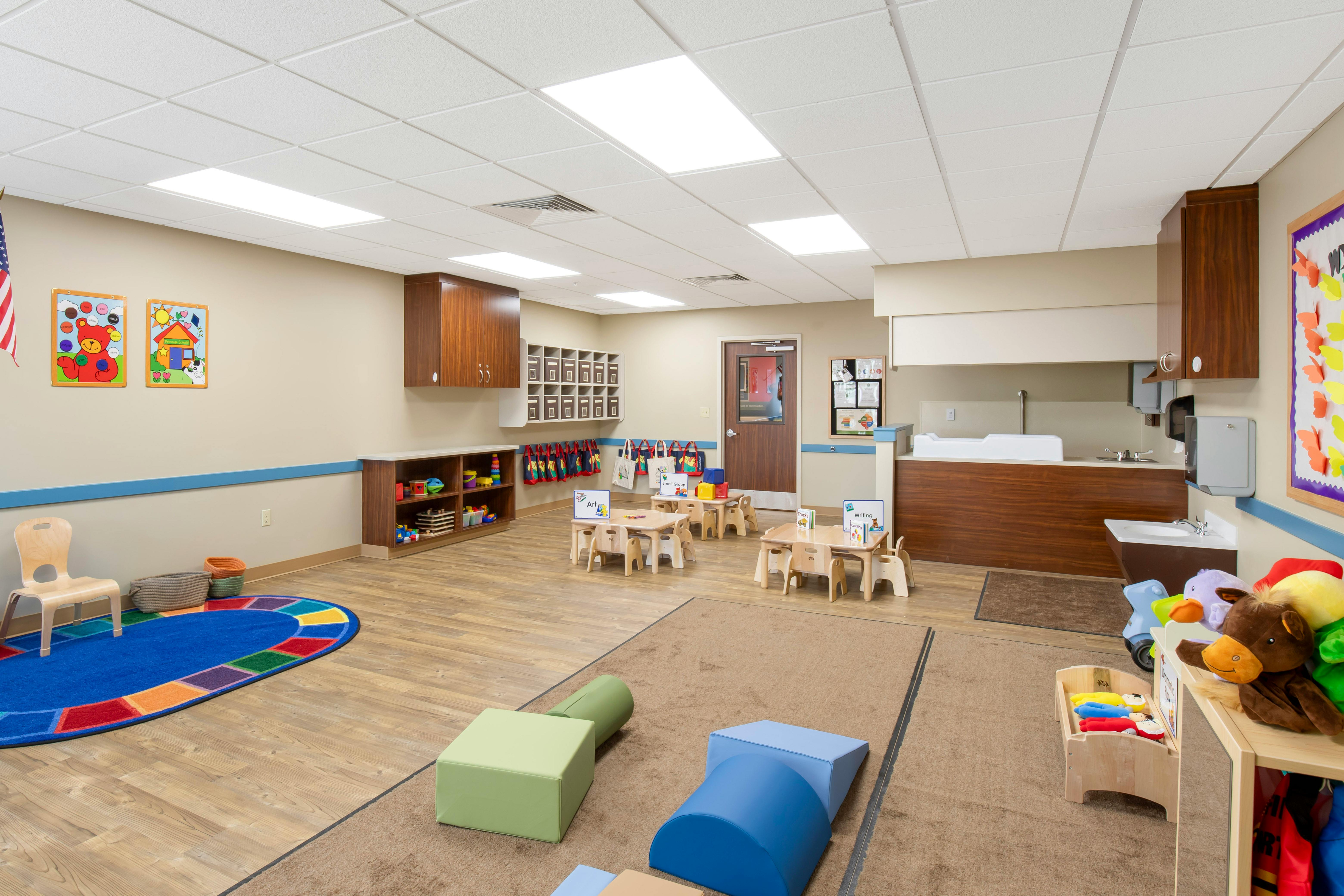 Classroom with small tables and chairs, play mats, and toys