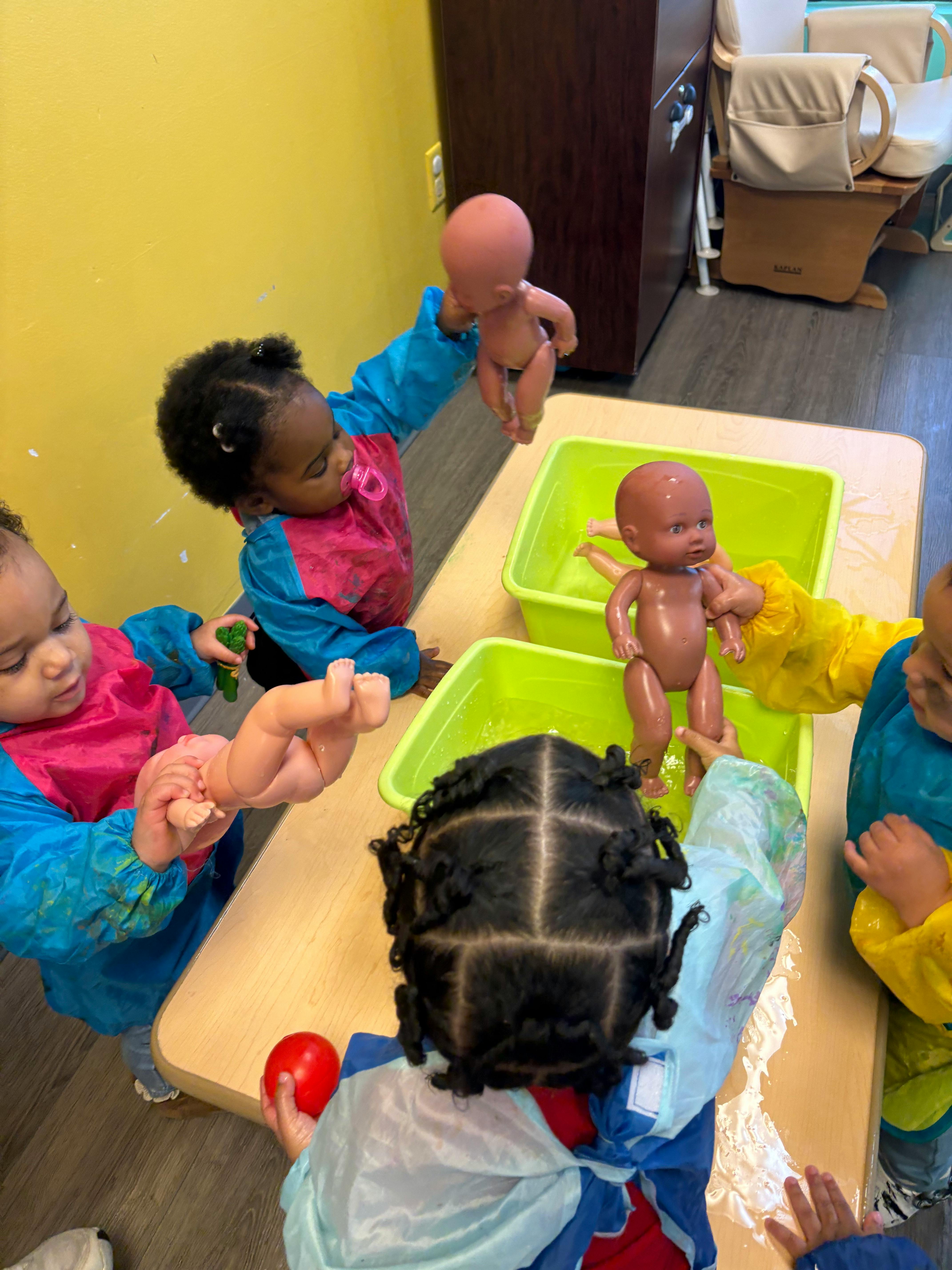 Children playing with dolls and water at a table
