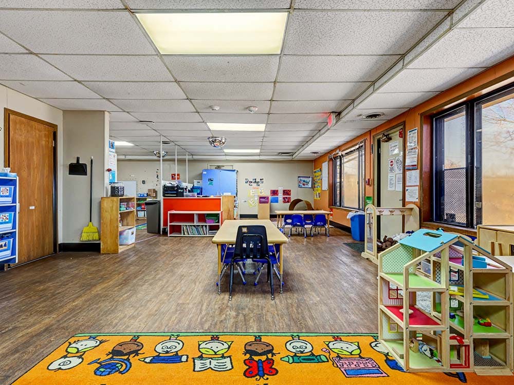 Childcare room with colorful rug, small tables, and shelves