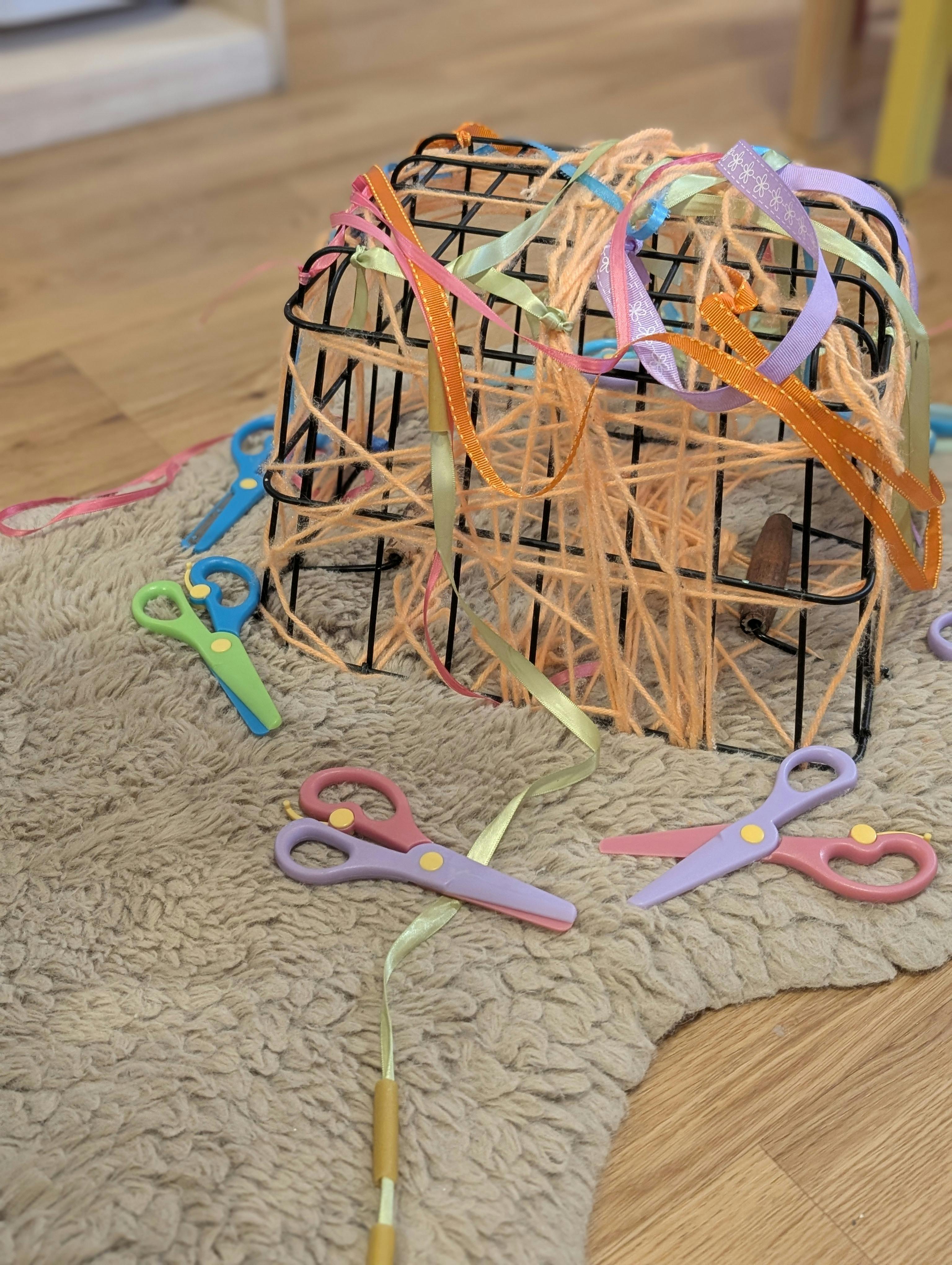 Small scissors surrounding a wire cage woven with yarn and ribbon