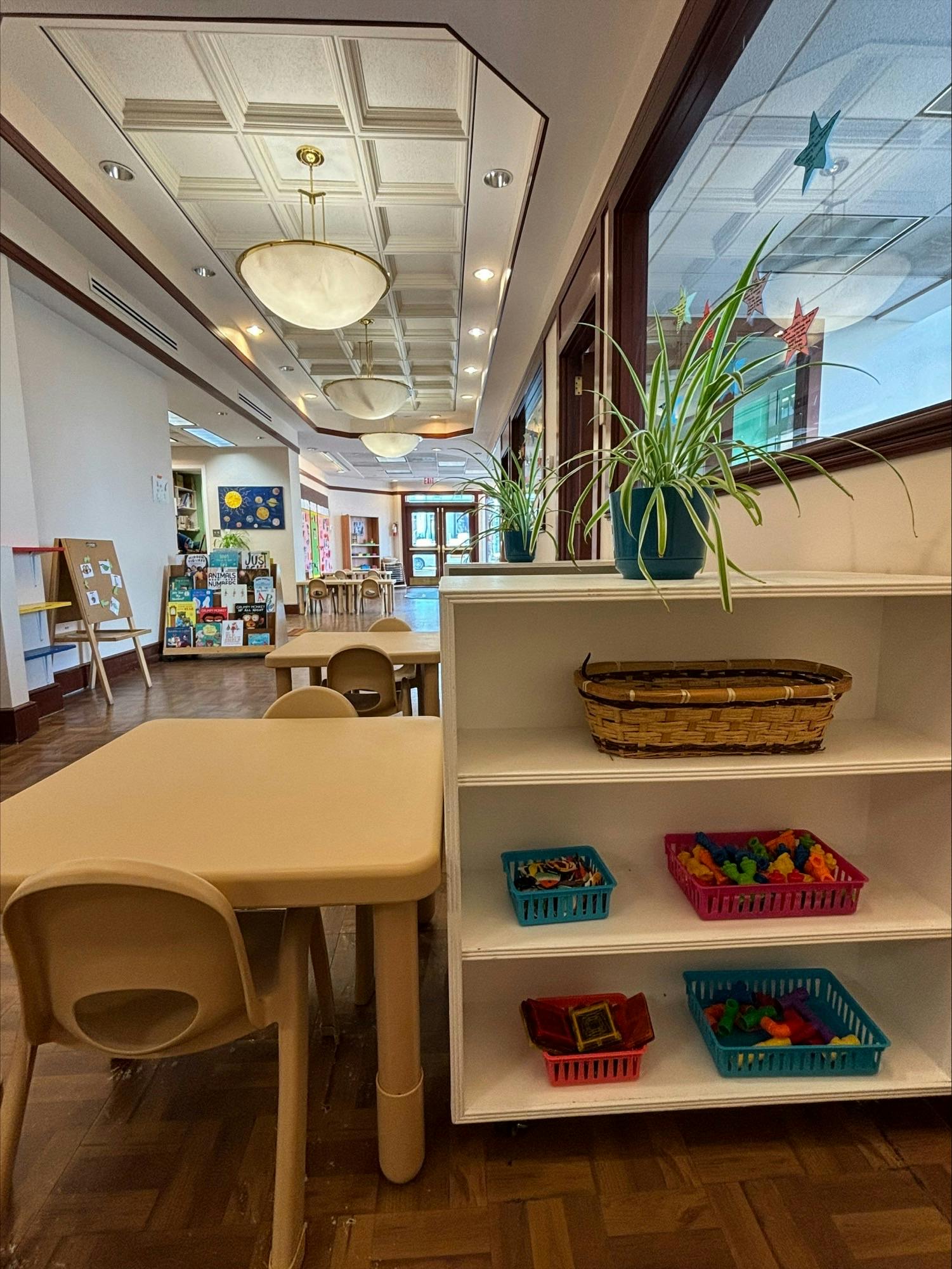Classroom with small tables and chairs, bookshelves, and plants