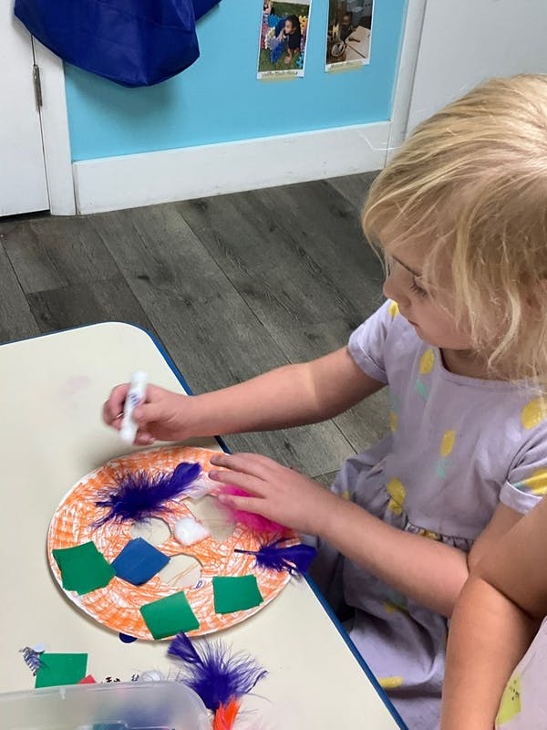 Child gluing feathers and paper shapes onto a paper plate
