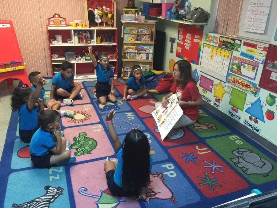 Adult reading to children sitting on a colorful alphabet rug in a classroom
