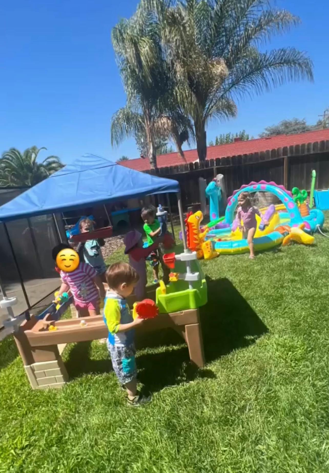 Children playing with water tables and an inflatable slide in a grassy yard