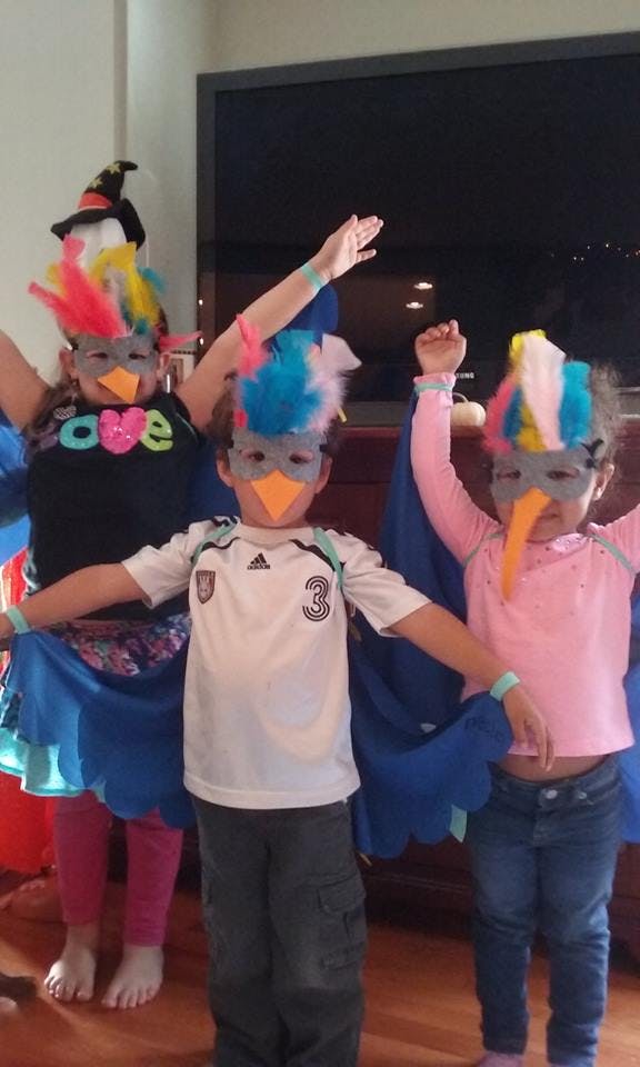 Three children in bird costumes with feathered masks and wings