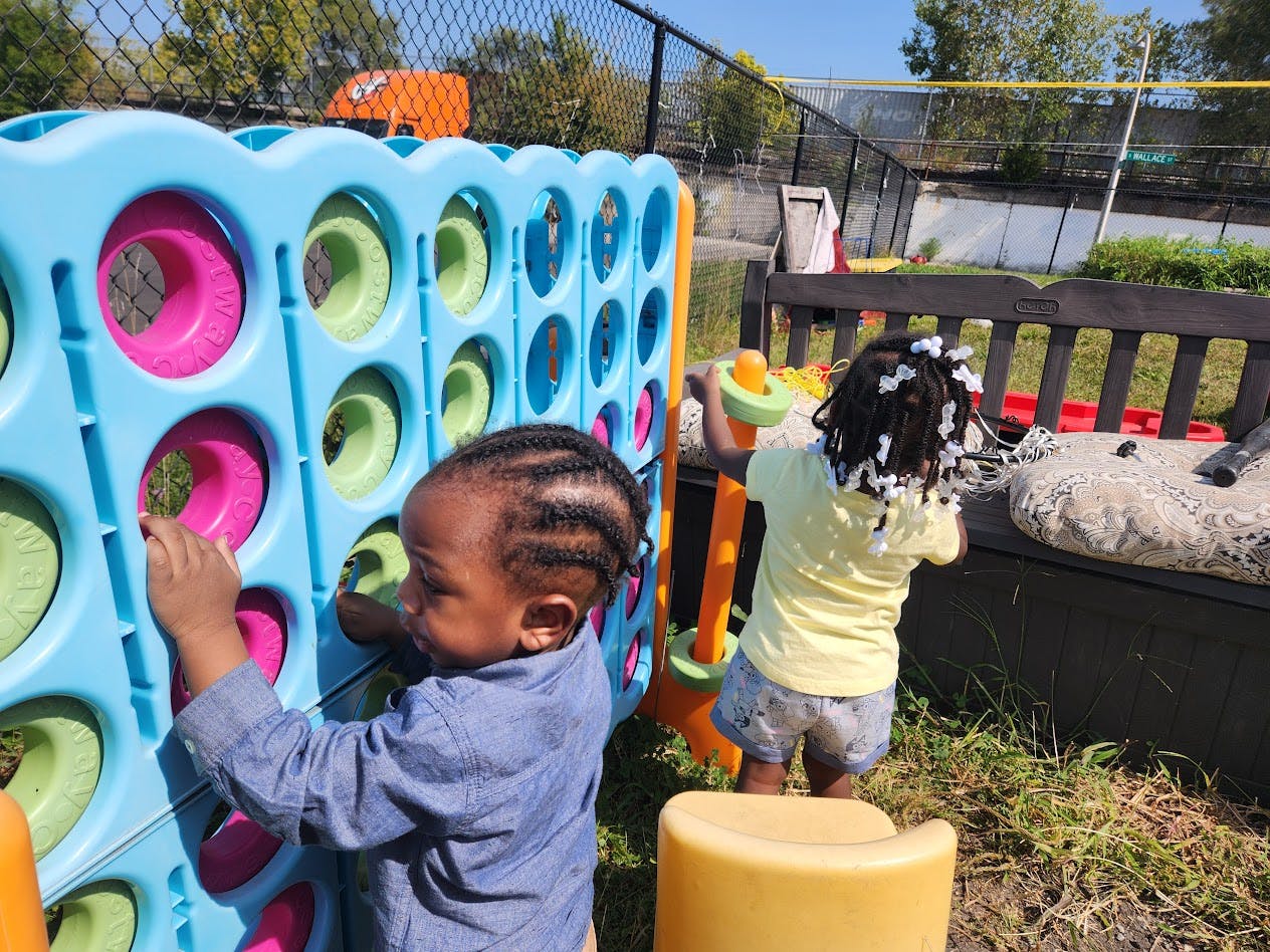 Two children playing with a large colorful connect four game outdoors