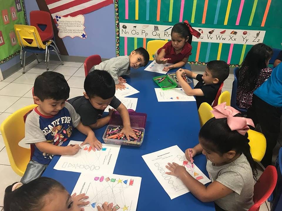 Children sitting at a table coloring on papers in a classroom