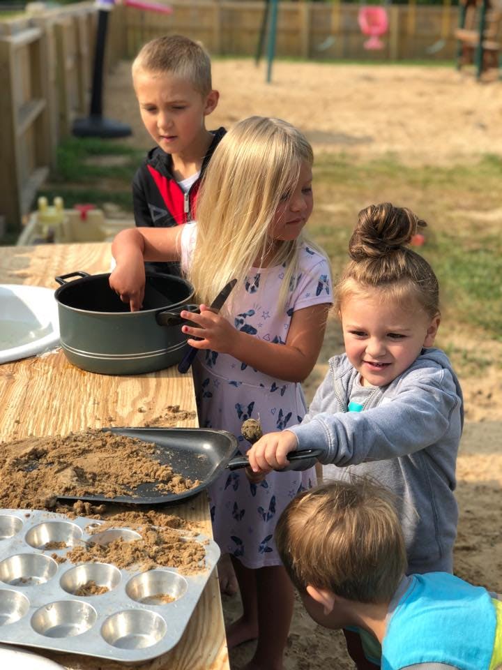 Children playing with sand and kitchen utensils outdoors