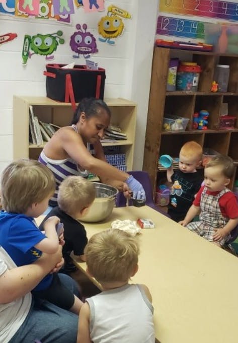 Person in a classroom mixing ingredients in a bowl with children watching