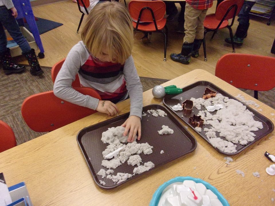 Child playing with kinetic sand on a tray at a table