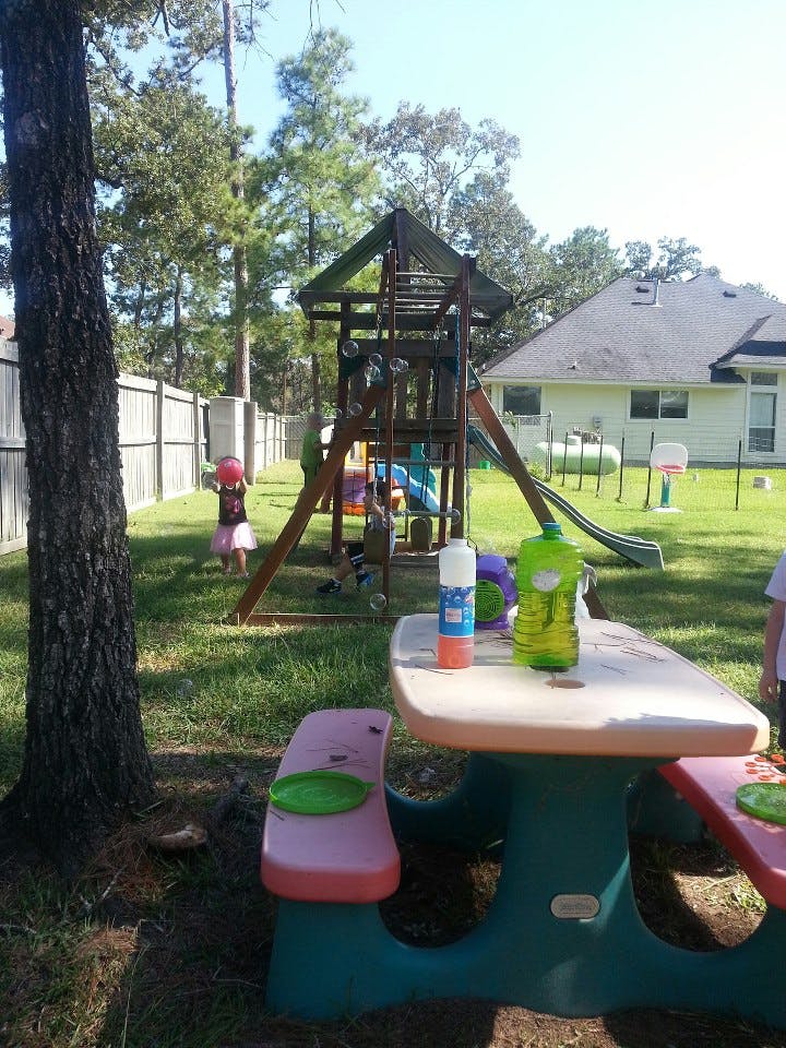 Child holding a red ball near a playground set in a backyard
