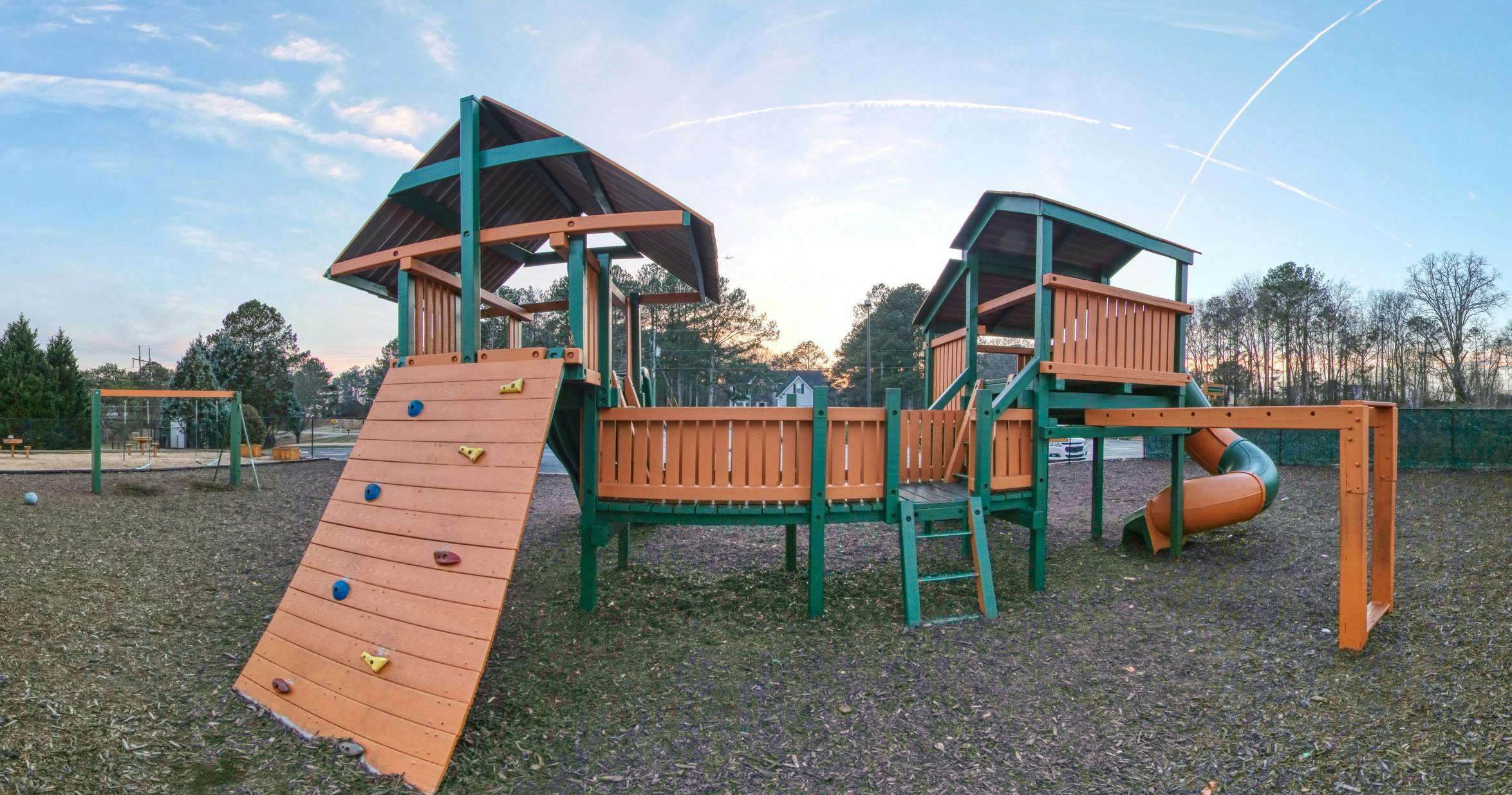 A wooden playground with a climbing wall, swings, and slides