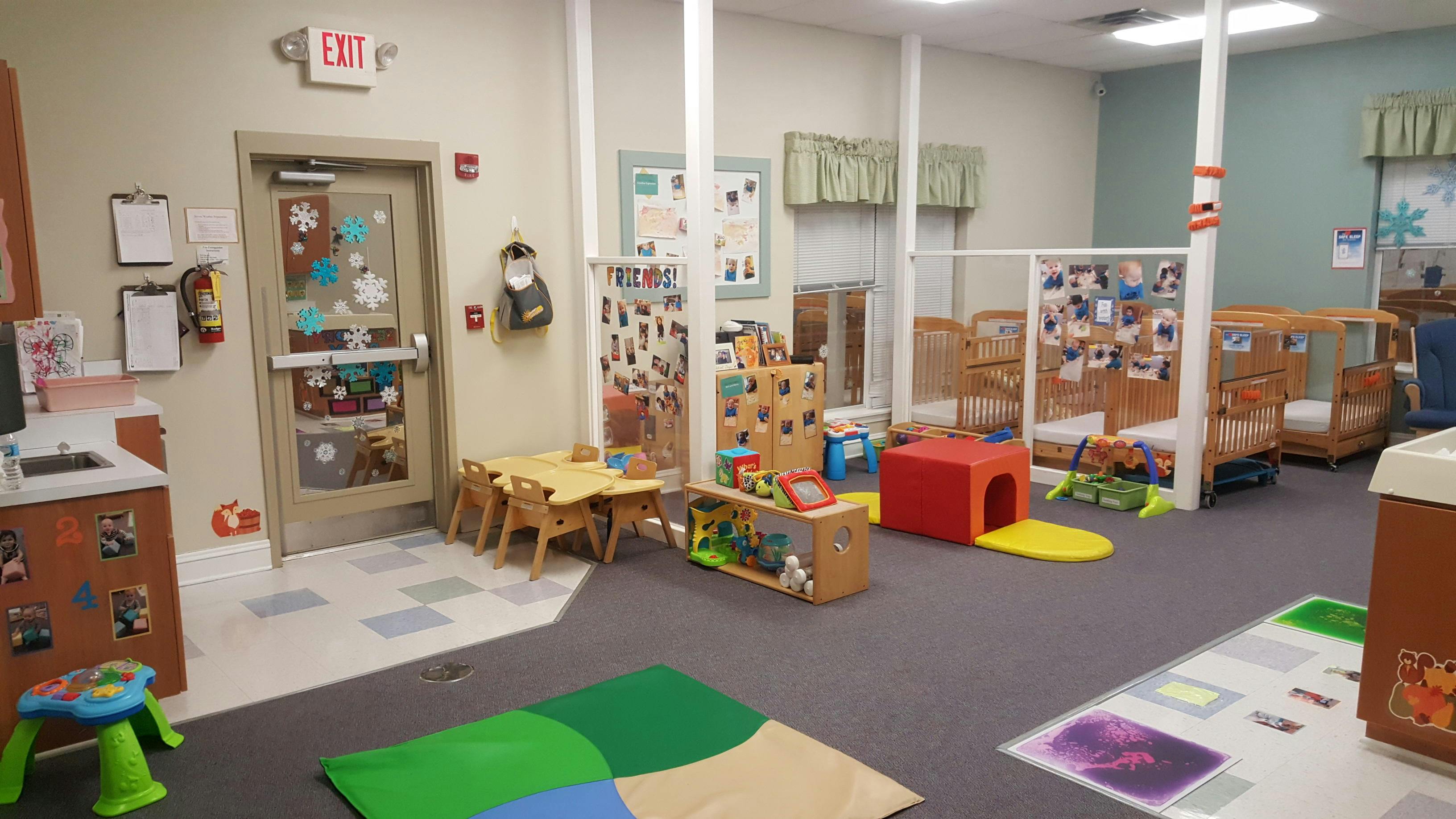 A colorful daycare room with cribs, small tables, and play mats