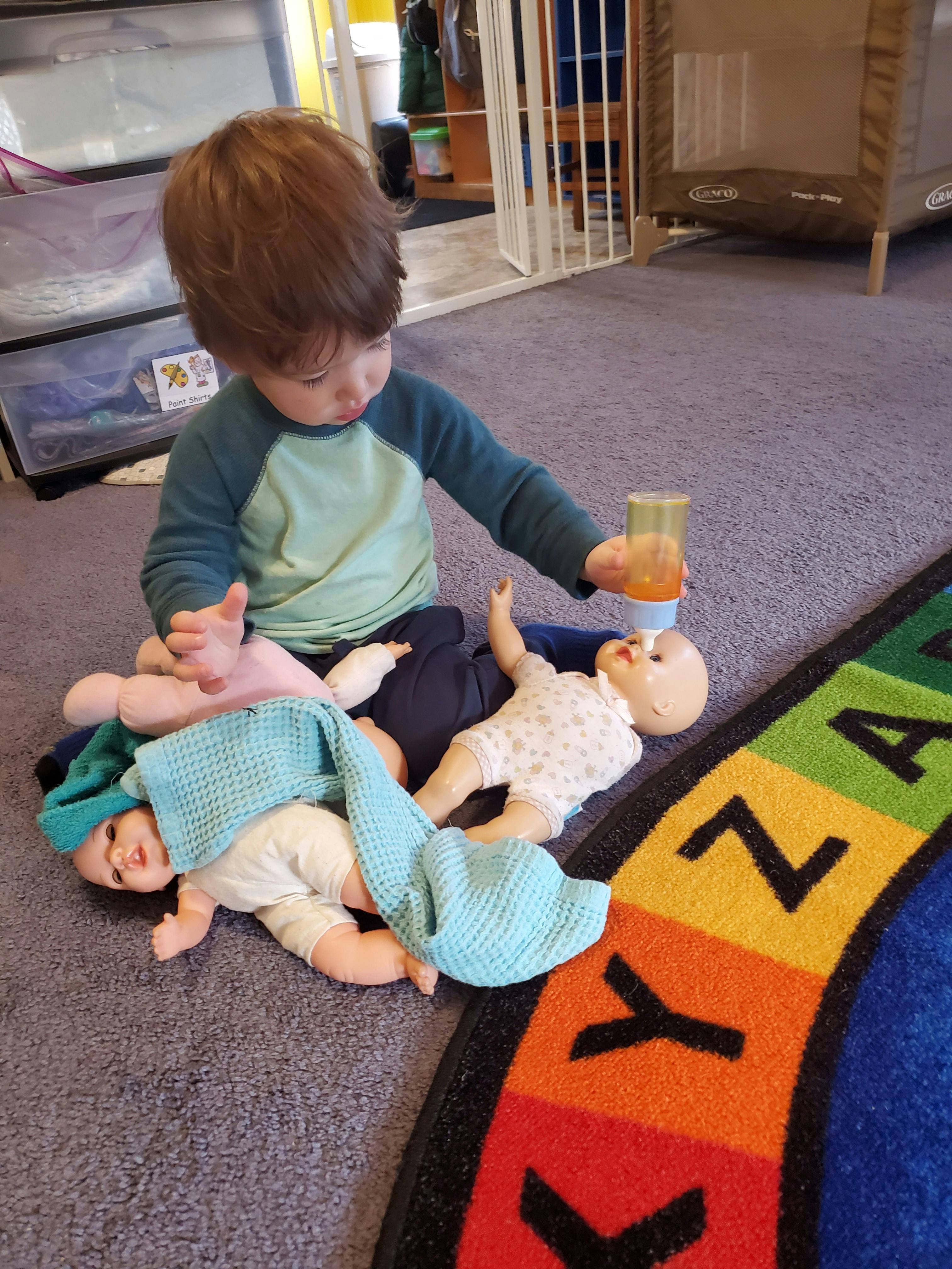 Child playing with dolls and a bottle on a rug