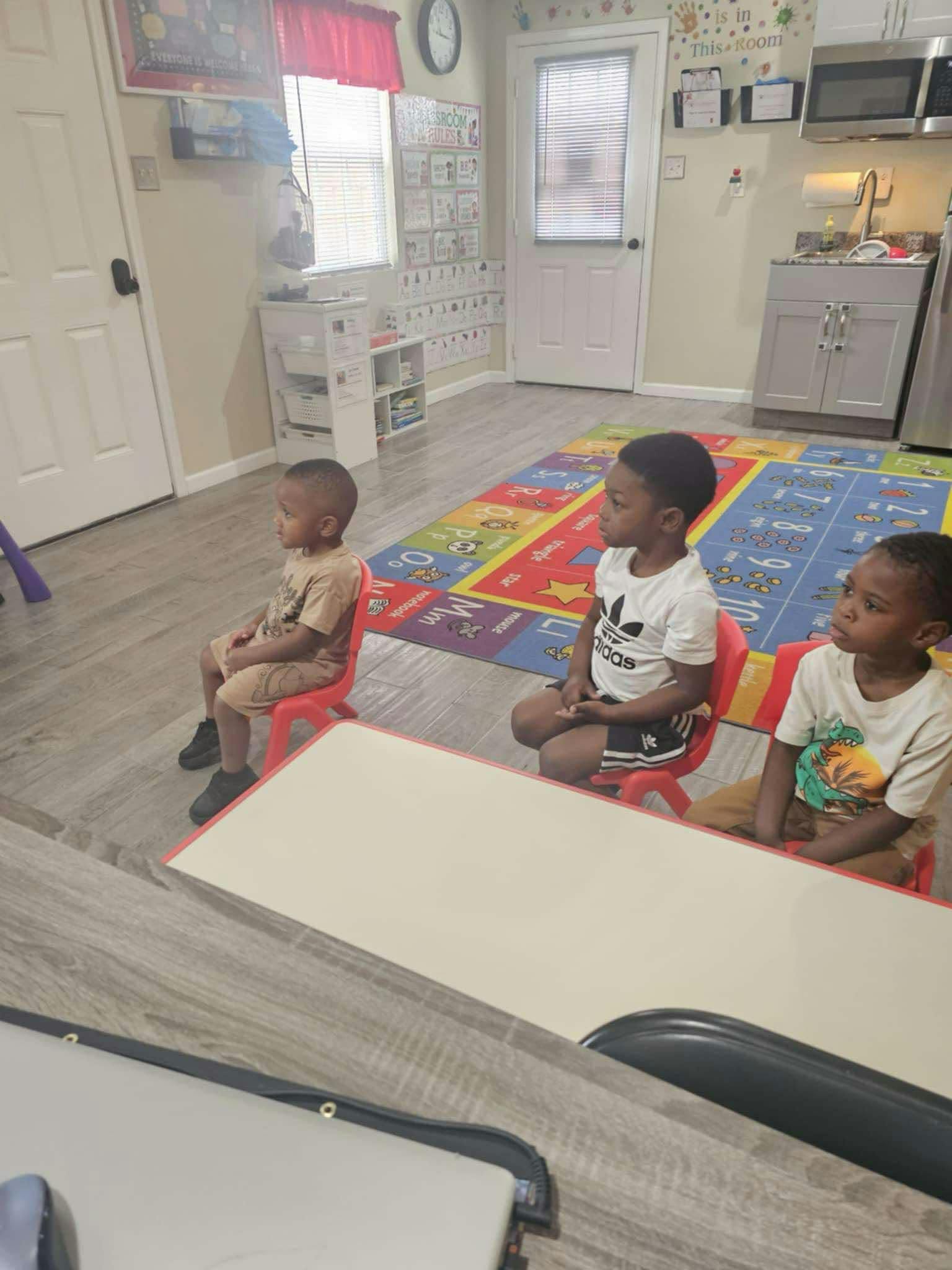 Three children sitting on red chairs in a room with a colorful rug