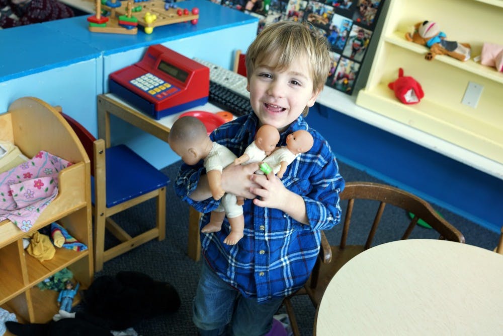 Child holding three dolls in a classroom