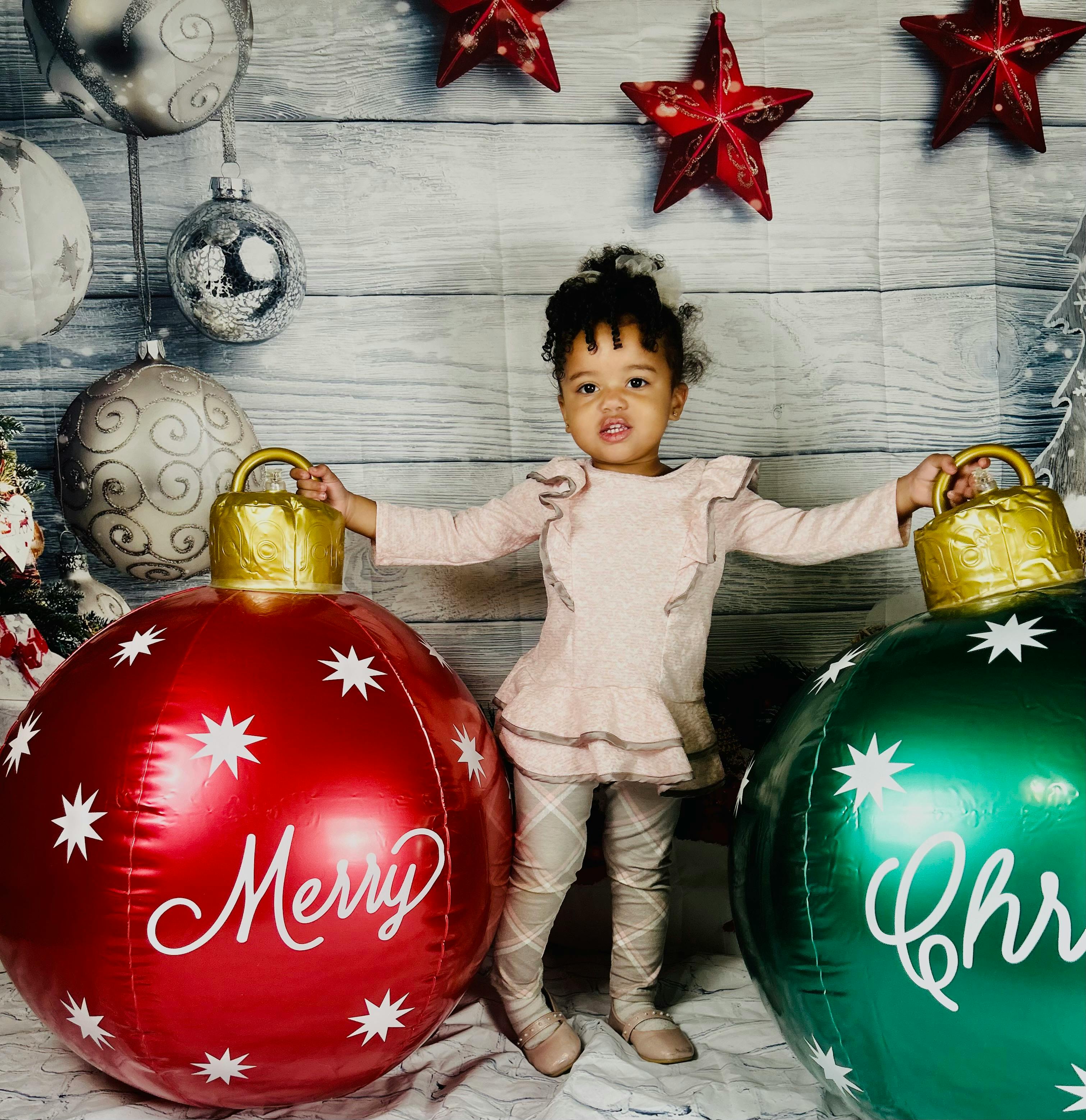 Child standing between two large Christmas ornaments, one red with "Merry"