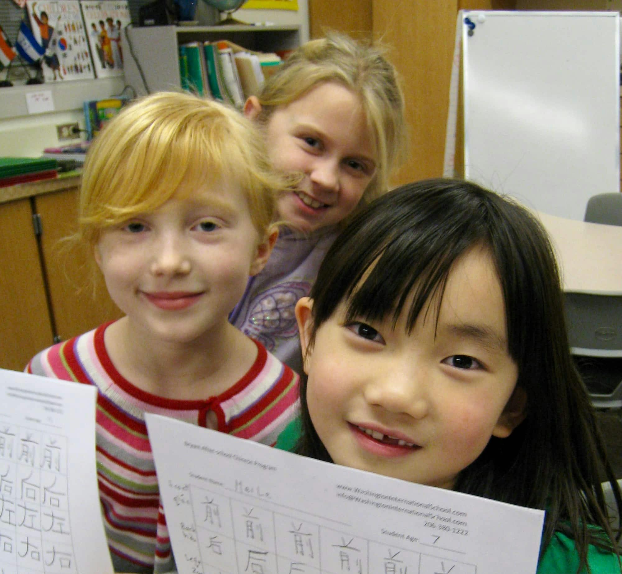 Three children holding papers with Chinese characters in a classroom