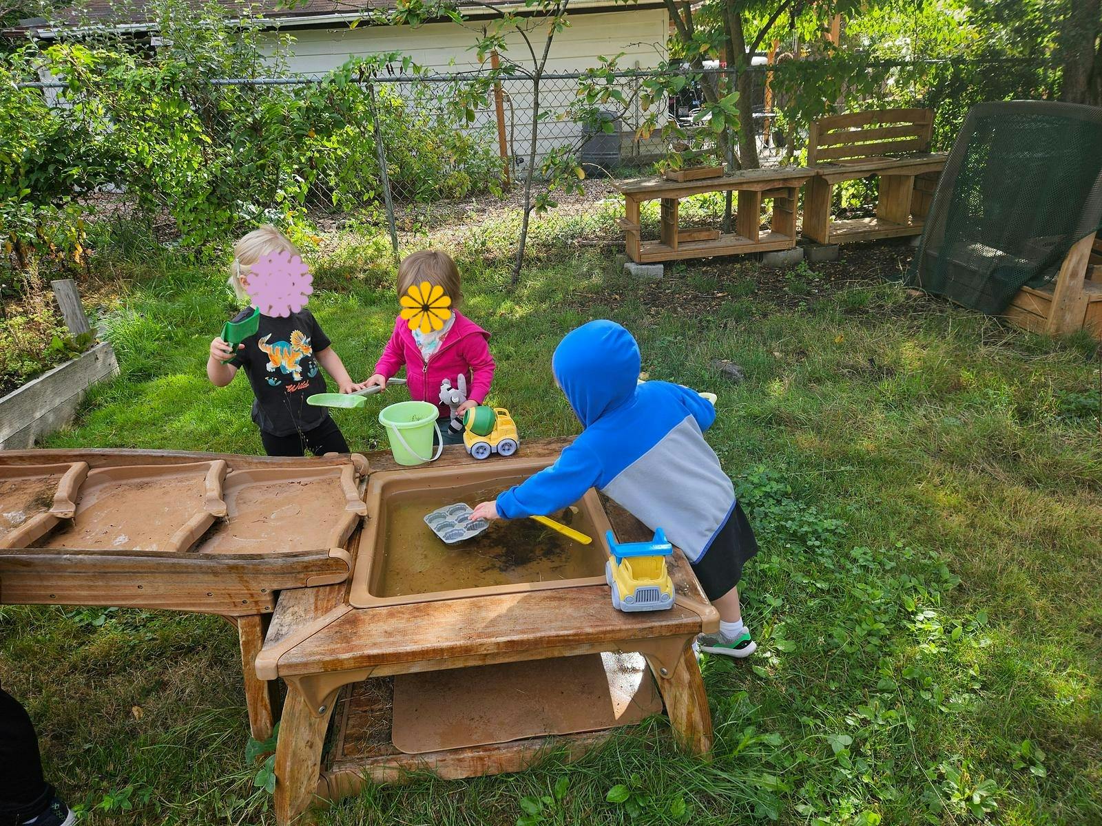 Three children playing outdoors with a mud table