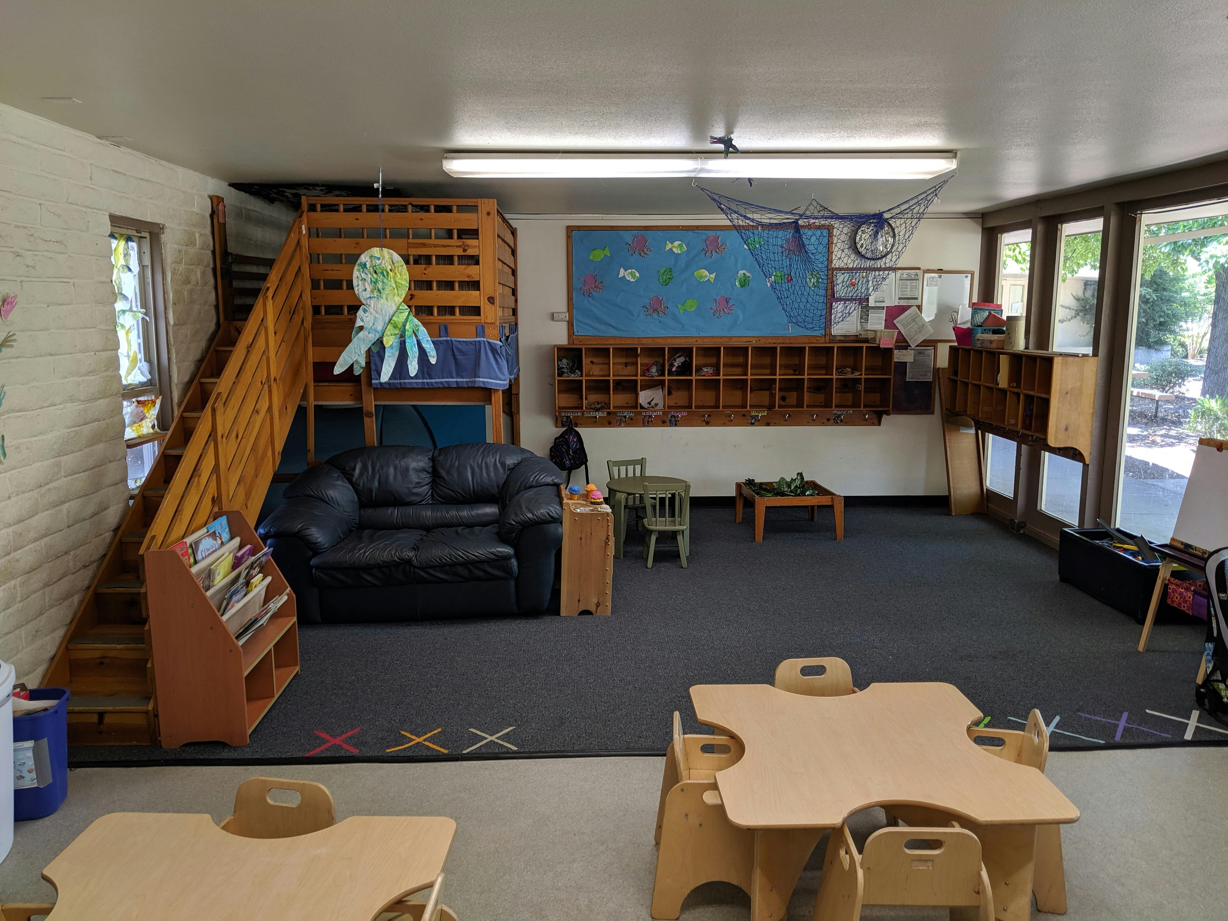 Indoor play area with a wooden play structure, black couch, and small tables