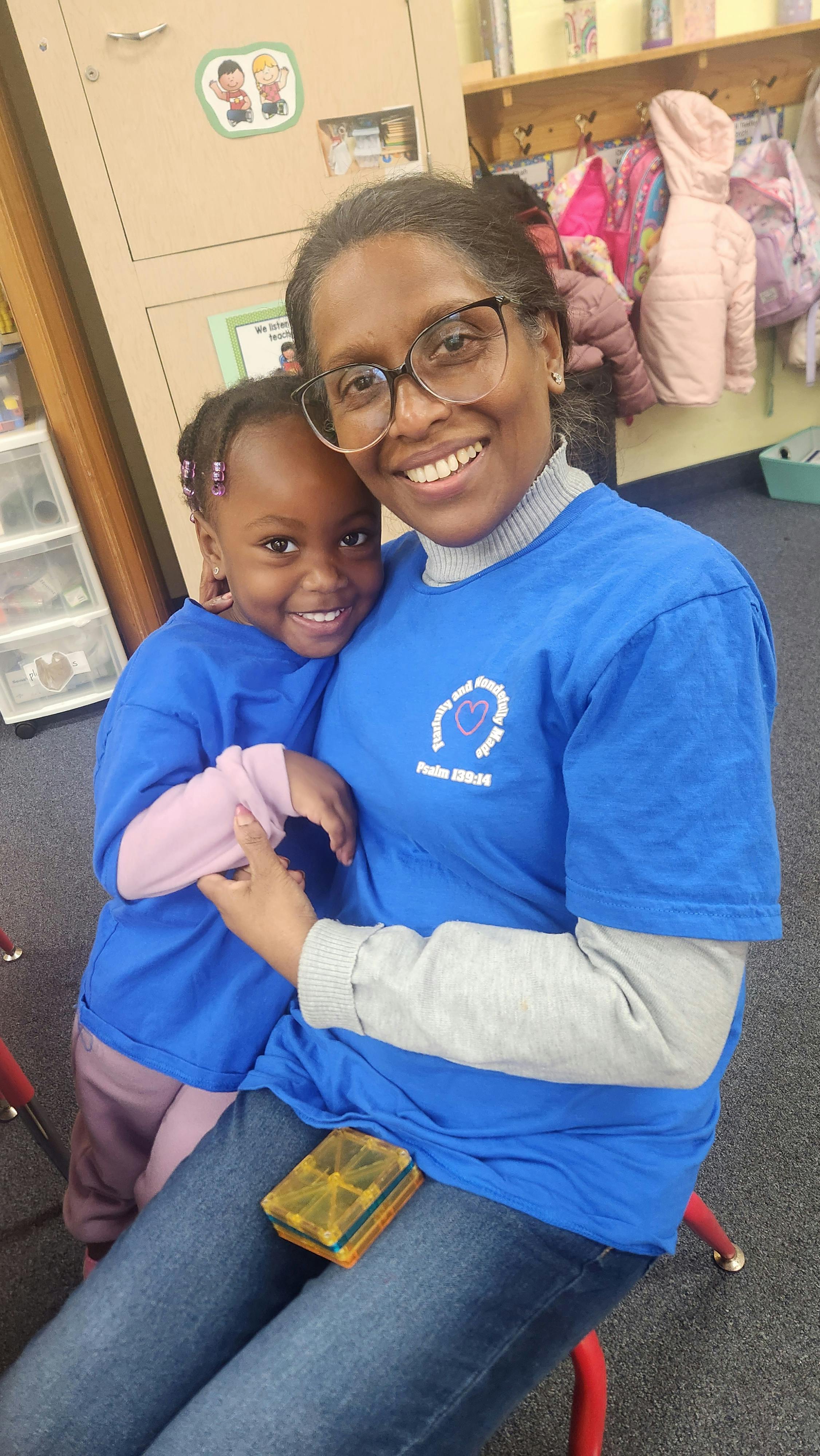 Person in glasses holding a child in a classroom