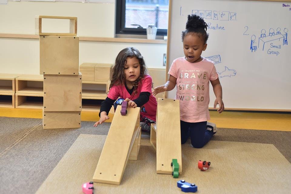 Two children playing with wooden ramps and toy cars in a classroom