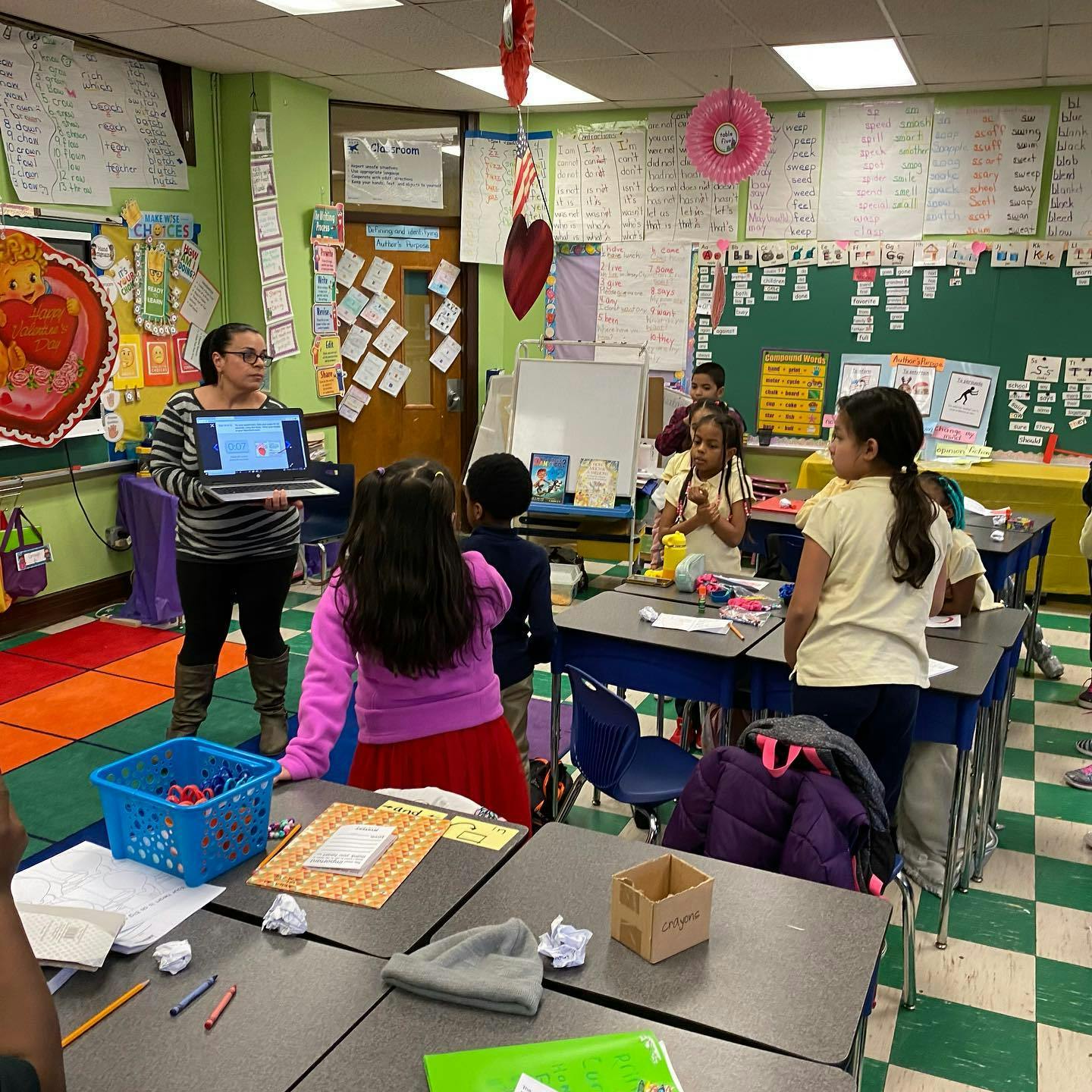 Person holding a laptop in a classroom with children