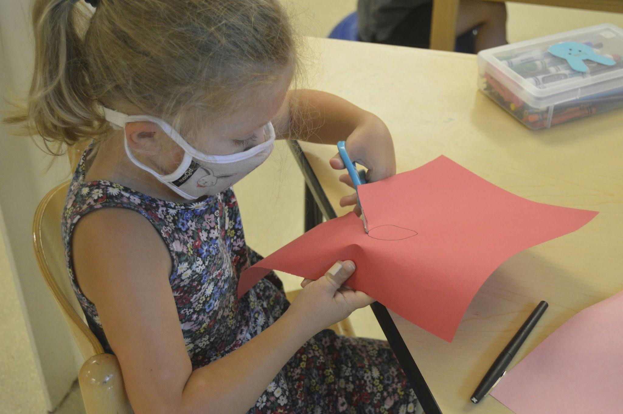 Child in a mask cutting red paper with scissors