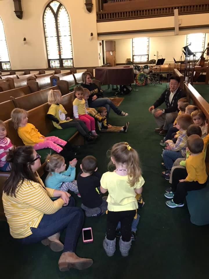 Adults and children sitting on the floor and pews in a large room