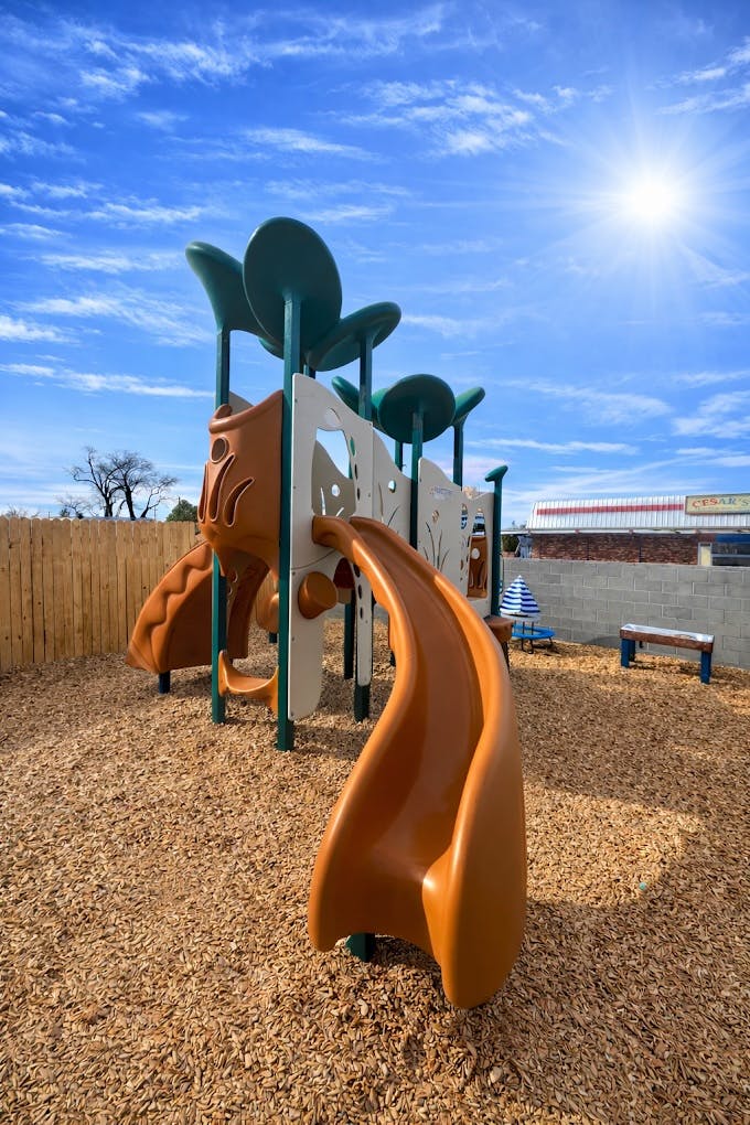 Playground structure with slides and climbing areas on wood chips under a sunny sky