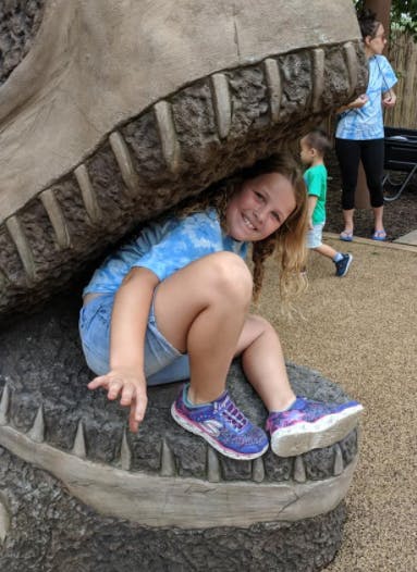 Child sitting inside a large dinosaur mouth structure
