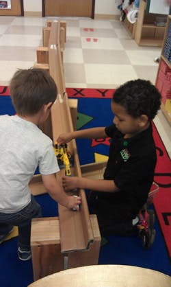 Two children playing with toy cars on a wooden track
